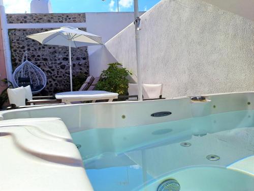 a bath tub with a table and an umbrella at Navita Cave Houses in Fira
