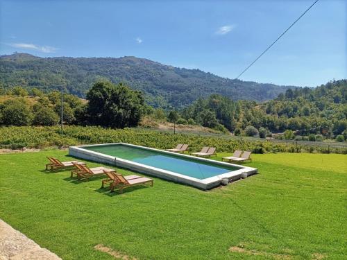 a swimming pool with chairs on a grass field at Quinta do Outeiro 1598 in Ponte da Barca