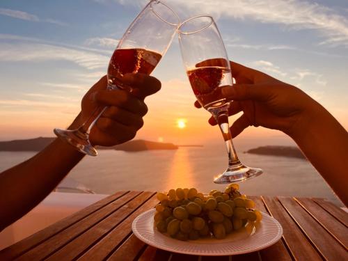 dos personas sosteniendo copas de vino y un plato de comida en Esmi Suites Santorini en Imerovigli