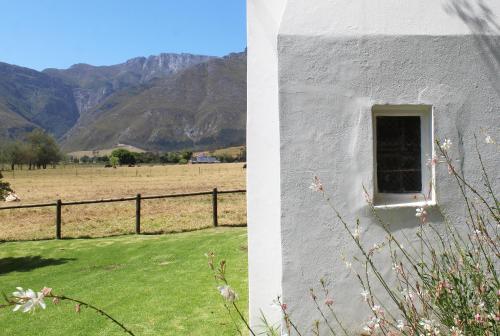 a building with a window and a field and mountains at Arumvale Country Retreat in Swellendam
