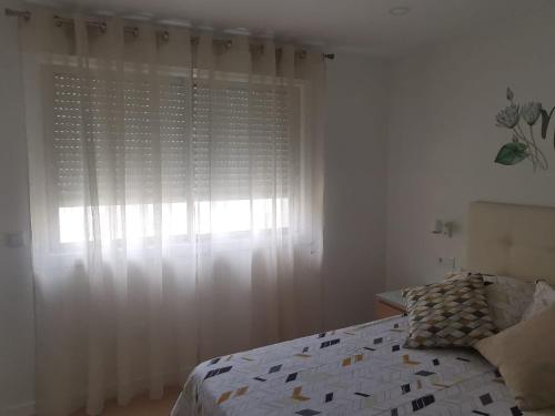 a bedroom with a bed and a window with white curtains at Ideal parejas in Moaña