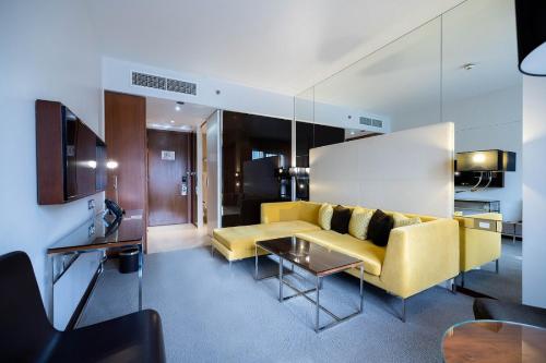 a living room with a yellow couch and a table at Centro Capital Doha - By Rotana in Doha