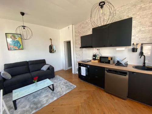 un salon avec un canapé noir et une cuisine dans l'établissement Grey Cosy, à Louviers