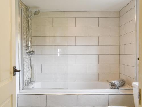 a white tub in a bathroom with white tiles at The Tallet Barn in Marhamchurch