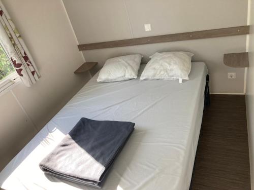 1 cama con sábanas blancas y almohadas en una habitación en Mobile home 3 chambres Camping Cœur de Vendée 3 étoiles, en La Boissière-de-Montaigu