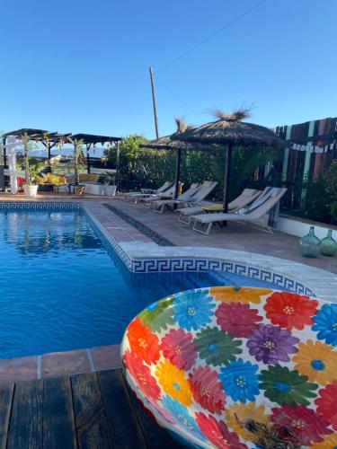 a pool with a colorful pillow next to some chairs and an umbrella at Glamping Bed and Breakfast Finca Alegria de la Vida in Pizarra