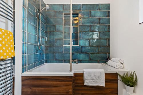 a bathroom with a tub with blue tiles at Woodfield House - Beautiful Tenby Cottage in Tenby