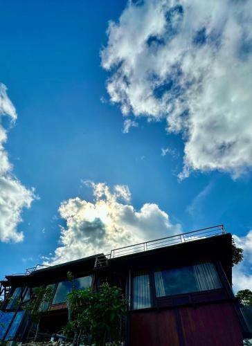 a building with a blue sky and clouds at Glamping Omah Kayu at Watu Paris Jogja in Girijati