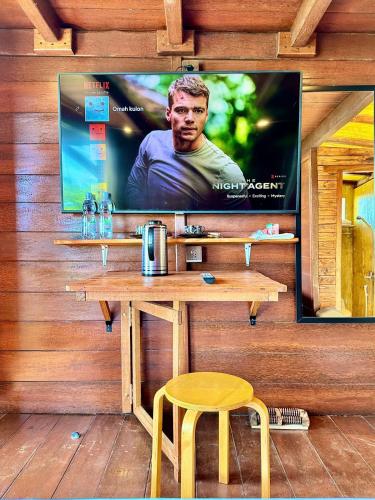 a television on a wall with a table and a stool at Glamping Omah Kayu at Watu Paris Jogja in Girijati