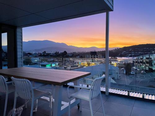 a table and chairs on a balcony with a sunset at Little Island Apartments in Hobart