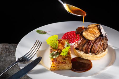 a white plate with a sandwich with meat and sauce at Lux Garden Hotel in Azuga