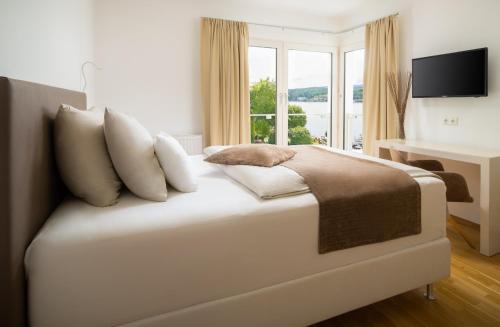 a white bedroom with a bed with pillows and a desk at Seehotel Europa Resort in Velden am Wörthersee