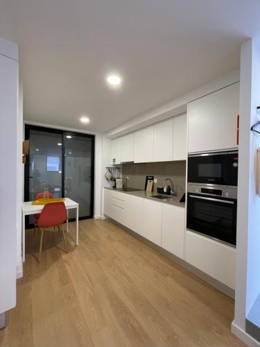 a kitchen with white cabinets and a red chair and a table at Living PDL 1 in Ponta Delgada