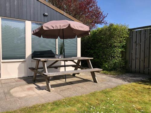 a picnic table with an umbrella in a yard at Comfortabel 6-persoons huisje nabij strand, bos, duinen en stad in Warmenhuizen