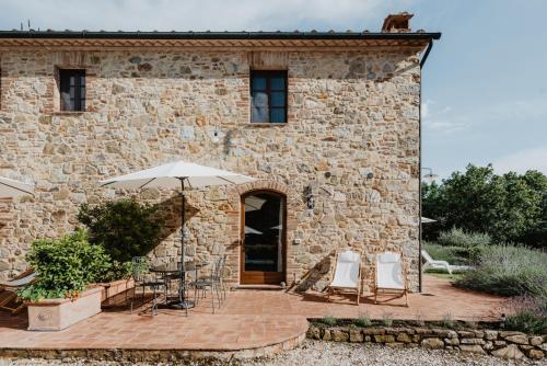 ein Steingebäude mit Stühlen und einem Regenschirm in der Unterkunft Borghetto Poggio Bianco in Radicondoli