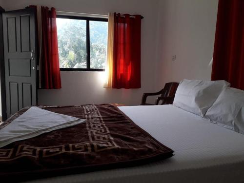 een slaapkamer met een bed met rode gordijnen en een raam bij MUNNAR FALCUNS in Anachal