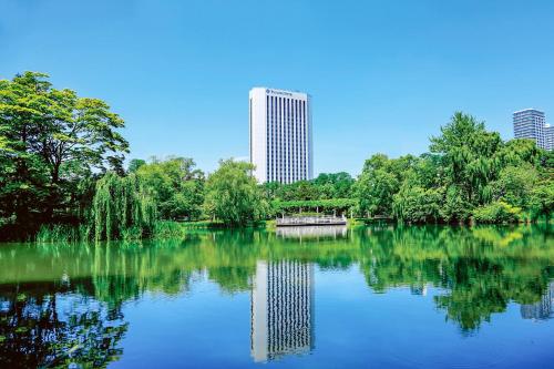Premier Hotel Nakajima Park Sapporo في سابورو: بركة في حديقة مع مبنى طويل في الخلفية