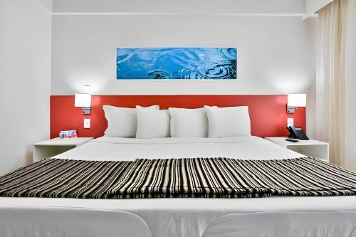 a bedroom with a large white bed with a red wall at True América apart-hotel in Campos dos Goytacazes