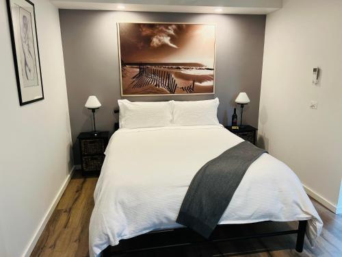 a bedroom with a large white bed with a painting on the wall at River cottage in Blairgowrie