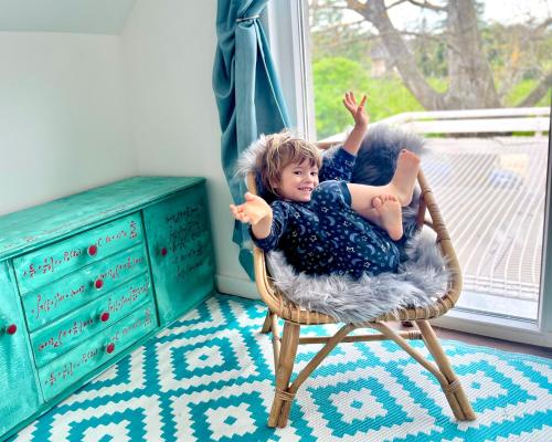 a young child sitting in a wicker chair in front of a window at Bohemian Eco lodge át lake Balaton in Kisapáti