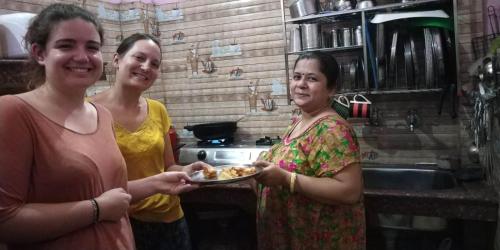 three women standing in a kitchen holding a plate of food at Azure Family Paying Guest House in Varanasi