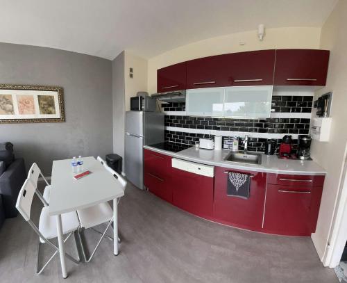 a kitchen with red cabinets and a white table at Appartement à 100m de la plage in Villers-sur-Mer