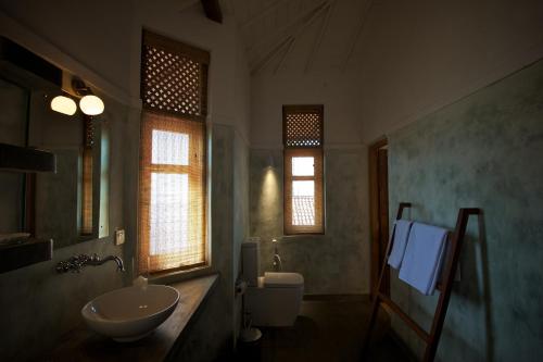 a bathroom with a sink and a toilet and windows at Jetwing Kottukal Beach House in Arugam Bay