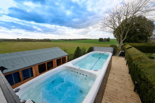 un grand bain à remous installé sur une terrasse à côté d'une maison dans l'établissement Luxurious 5-Bed House with Pool, Hot Tub & Parking, à Eastry