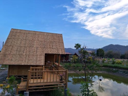 a house with a thatched roof next to a pond at คูณ-เนื่อง ฟาร์ม สเตย์ หัวหิน Koon & Nueang Farm Stay Hua Hin in Ban Bo Fai