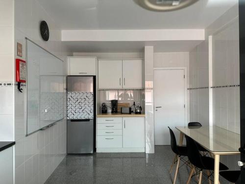 a kitchen with white cabinets and a table and a refrigerator at Conforto, espaço e localização in Ribeira Grande
