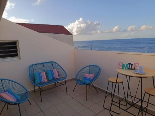 Un balcón con sillas, una mesa y el océano en Cibuqueira numéro 7, Centre ville, vue sur mer , plage à pied, en Le Moule