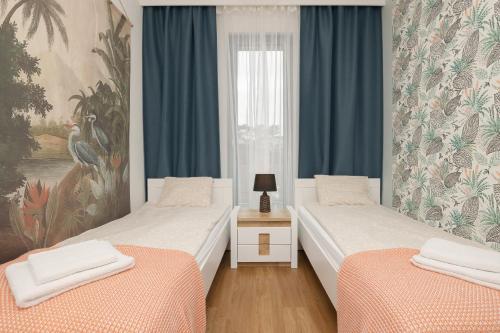 2 łóżka w pokoju z niebieskimi zasłonami i oknem w obiekcie Sea&Sky View Apartment Par La Mer w mieście Niechorze