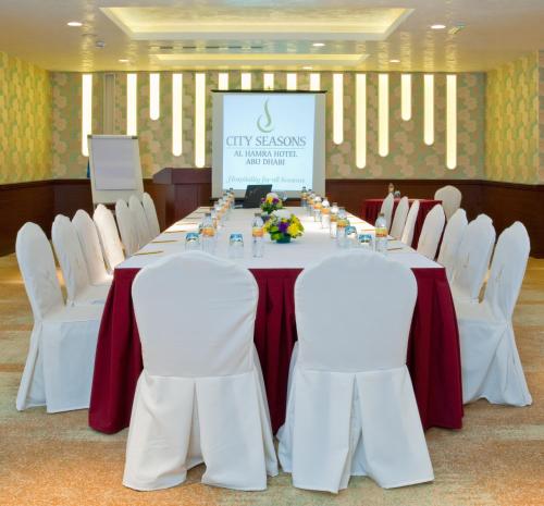 a long table with white chairs and a screen at City Seasons Al Hamra Hotel in Abu Dhabi