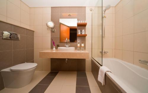 a bathroom with a toilet and a sink and a tub at City Seasons Al Hamra Hotel in Abu Dhabi