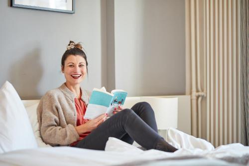 a woman sitting on a bed reading a book at Kurhaus Lenzerheide in Lenzerheide