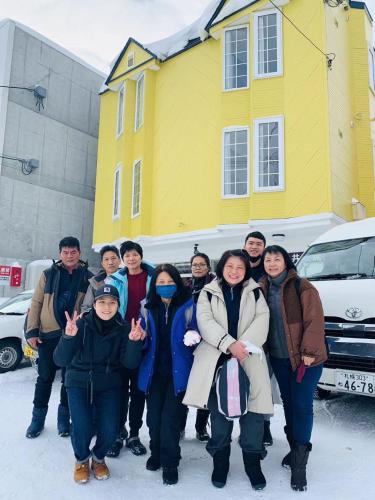 a group of people posing in front of a yellow house at Warm House1 in Sapporo