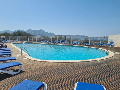 une grande piscine avec des chaises longues bleues sur une terrasse dans l'établissement Appartement Vue Mer, piscine, minigolf, parking, à Lumio