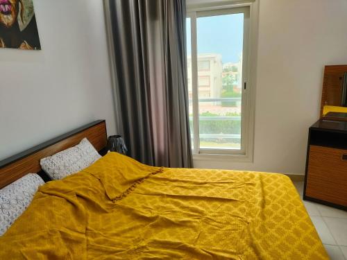 a bedroom with a yellow blanket on a bed with a window at قريه امواج الساحل الشمالي in El Alamein
