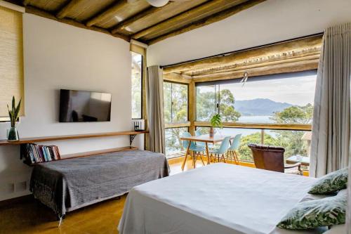 Un dormitorio con una cama y un balcón con una mesa. en OPN - Ora pro Nóbis Guest House, en Ilhabela