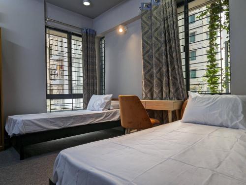 a room with two beds and a chair and windows at GreyRooms in Dhaka