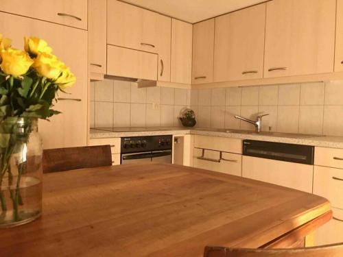 Cosy apartment in heritage protected swiss chalet في ماتين: مطبخ مع طاولة خشبية و مزهرية من الورود الصفراء
