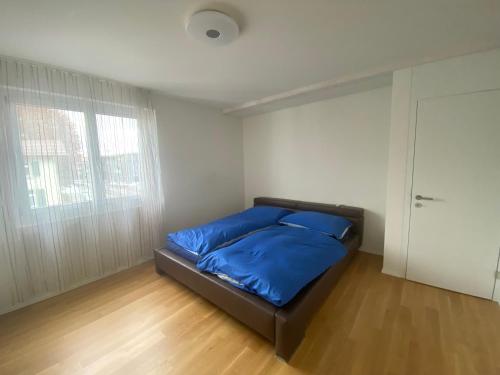 Schlafzimmer mit einem Bett mit blauer Bettwäsche und einem Fenster in der Unterkunft Minergie in Rickenbach