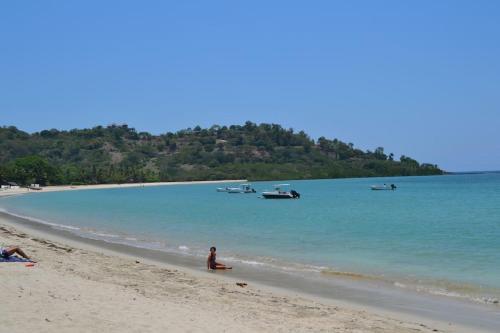 a person sitting on a beach with boats in the water at Superbe villa avec ponton privé in Andilana
