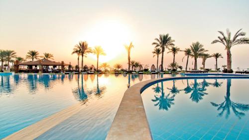 a swimming pool with palm trees and the sunset at Sunrise Montemare Resort -Grand Select in Sharm El Sheikh