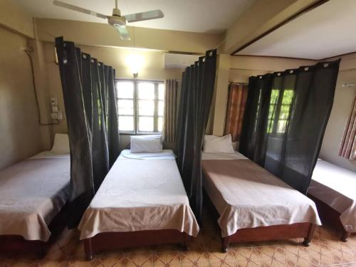 three beds in a room with a ceiling fan at Manilath guesthouse in Ban Houayxay