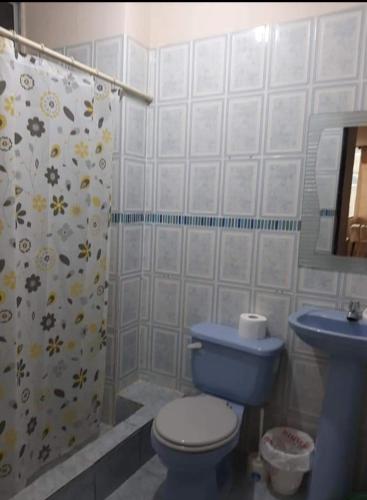La salle de bains est pourvue de toilettes bleues et d'un rideau de douche. dans l'établissement Departamentos de la Costa, à Machala