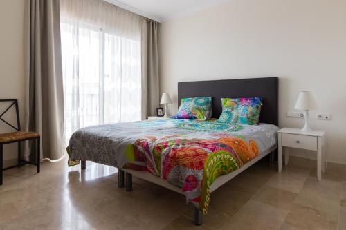 Un dormitorio con una cama con un edredón colorido y una ventana en Luxe appartement Las Palmeras Calahonda, en Sitio de Calahonda