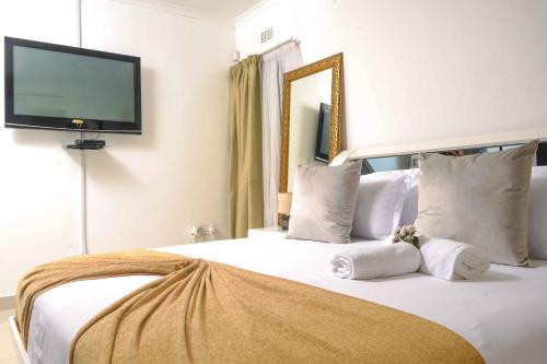 a bedroom with a large white bed with a flat screen tv at acaciaoptimumstay in Gaborone