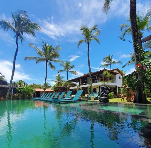uma piscina num resort com cadeiras e palmeiras em Pousada Casa da Praia em Caraíva