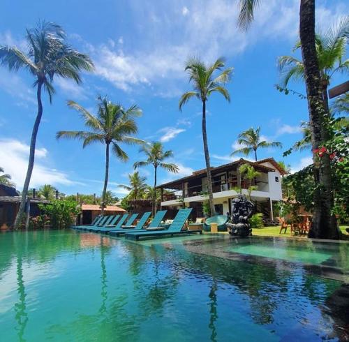 a pool at a resort with chairs and palm trees at Pousada Casa da Praia in Caraíva